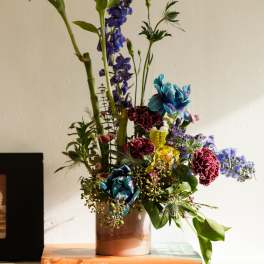 Tall mixed flower arrangement with blue, red, and yellow blooms in a ceramic vase on an orange book.