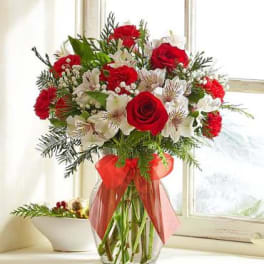 Red roses and white flowers in a clear glass vase with a red ribbon