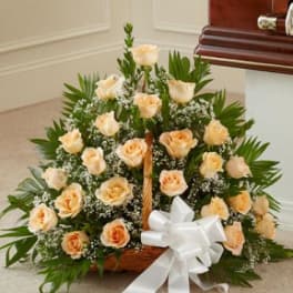 Peach roses arranged in a basket with a white ribbon bow