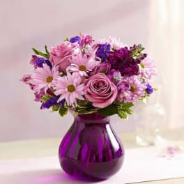 Pink and purple mixed bouquet in a purple glass vase