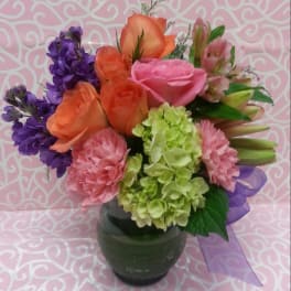 Mixed bouquet of roses, carnations, hydrangea, and purple blooms in a glass vase
