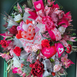 Heart-themed wreath with pink and red flowers, ribbons, and a "Be Mine" sign