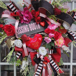 Heart-shaped floral wreath with red and pink roses and a "Kissing Booth" sign