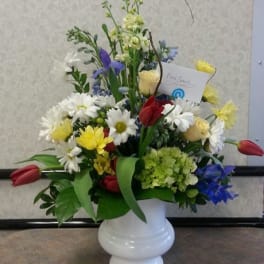 Mixed bouquet of daisies, tulips, and roses in a white vase