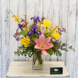 Mixed bouquet with pink lily, yellow daffodils, and purple iris in a glass vase