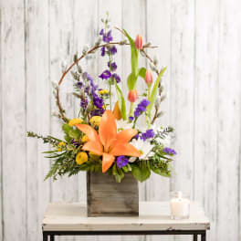 Orange lily bouquet with purple and white flowers in a wooden box