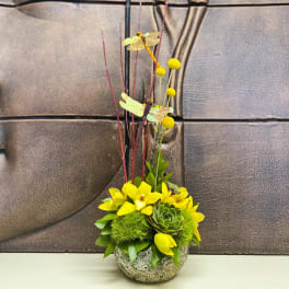 Yellow floral arrangement in a round stone bowl with tall decorative stems