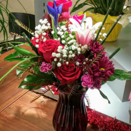 Mixed bouquet of roses, lilies, and daisies in a dark glass vase