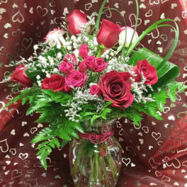 Red and pink roses arranged in a glass vase with heart-patterned wrap