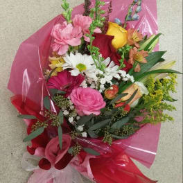 Mixed bouquet of pink, red, yellow, and white flowers wrapped in pink paper