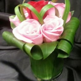 Small bouquet of pink and red roses wrapped with green ribbon loops