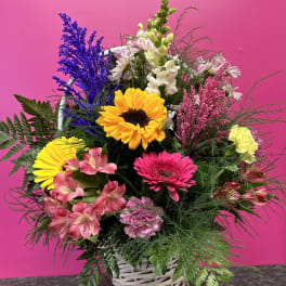 Mixed bouquet with sunflowers, gerbera daisies, and pink blooms in a white basket