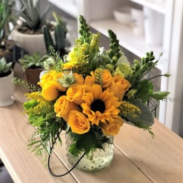 Yellow roses and a sunflower in a clear glass vase