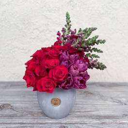 Red roses and purple flowers arranged in a gray vase