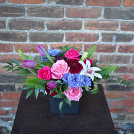 Mixed bouquet in a black square vase with pink, purple, blue, and white flowers