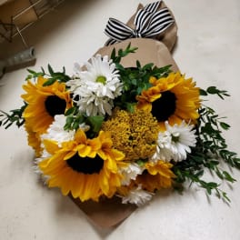 Bouquet of sunflowers, white daisies, and yellow filler flowers wrapped in brown paper