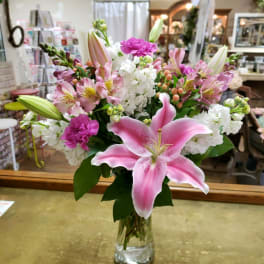 Pink lilies and mixed flowers arranged in a clear glass vase