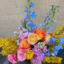 Handheld bouquet of orange and pink roses with blue and purple flowers