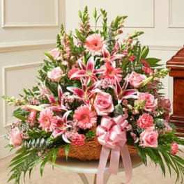 Pink floral arrangement in a wicker basket with a ribbon bow
