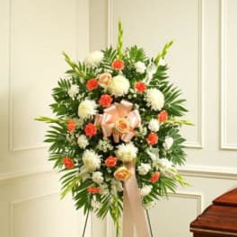 Standing floral wreath with white and coral flowers and a pink ribbon