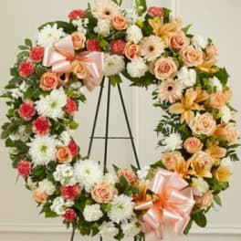 Large floral wreath with peach roses, white mums, and pink carnations on a stand