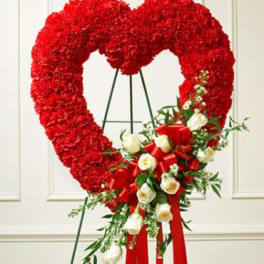 Heart-shaped red floral wreath on an easel with white roses and red ribbon