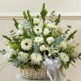 White floral arrangement in a wicker basket with a white ribbon