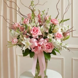 Pink roses and white lilies in a clear glass vase with a pink ribbon