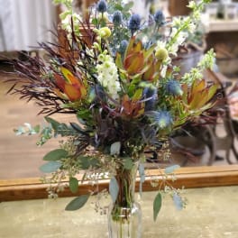 Mixed floral arrangement in a clear glass vase with blue thistle and orange protea