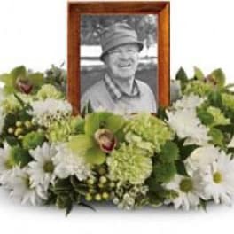 White daisy and green floral tribute around a framed photo