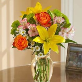 Bouquet of yellow lilies, orange roses, and pink alstroemeria in a glass vase