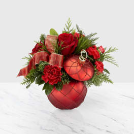 Red roses and carnations arranged with Christmas ornaments in a low container