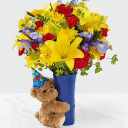 Bouquet of yellow, red, and purple flowers in a blue vase with a teddy bear