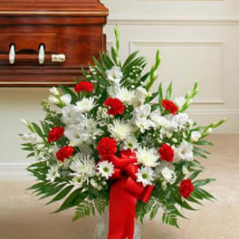 Red and white funeral spray with a red ribbon beside a casket