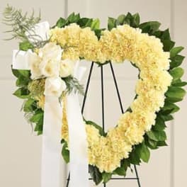 Heart-shaped floral wreath with yellow flowers and a white ribbon on a stand