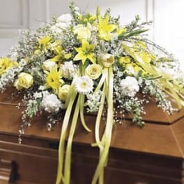 Yellow and white funeral spray on a wooden casket