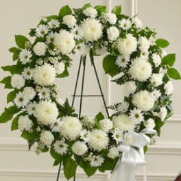 White floral wreath on a black stand with a white ribbon