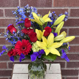 Bouquet of red roses, yellow lilies, and blue flowers in a glass vase