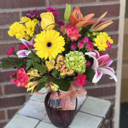 Bright mixed bouquet in a purple vase with a butterfly accent