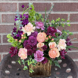 Mixed bouquet of peach, pink, and purple flowers in a brown vase