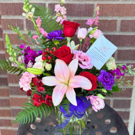 Mixed bouquet with red roses, pink lilies, and purple flowers in a glass vase