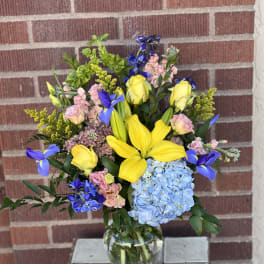 Mixed bouquet with yellow lilies, blue hydrangea, and pink flowers in a glass vase