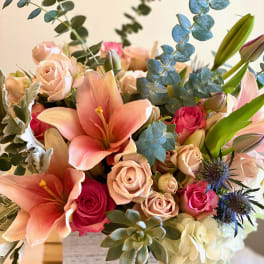 Bouquet of peach lilies, pink roses, and eucalyptus in a vase