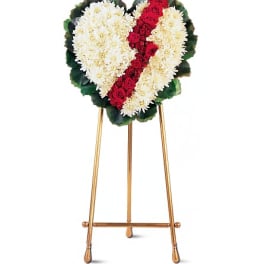 Heart-shaped funeral wreath of white flowers with a red rose stripe on a stand