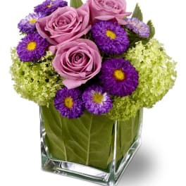 Pink roses and purple daisies in a clear square vase
