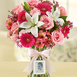 Pink and white bouquet in a glass vase with a baby photo frame