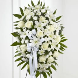 White floral standing spray with roses and lilies on a white ribboned easel