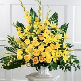 Yellow floral arrangement in a white vase with broad green leaves