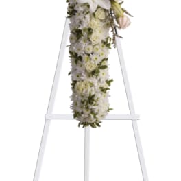 White floral cross on a stand with lilies and roses