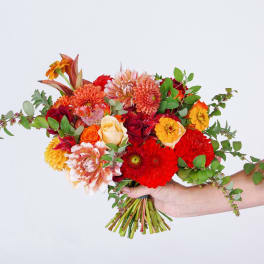 Handheld bouquet of red, orange, and cream flowers with greenery